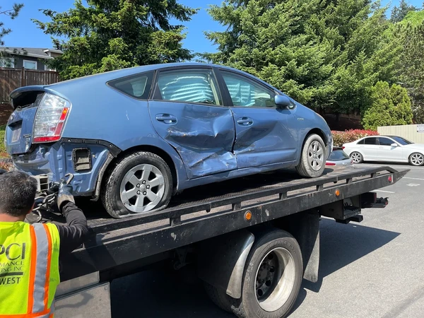 Damaged blue Toyota Prius secured on a flatbed tow truck