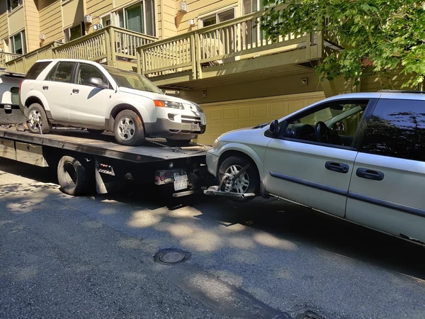 Flatbed carrying a white SUV while towing a silver minivan
