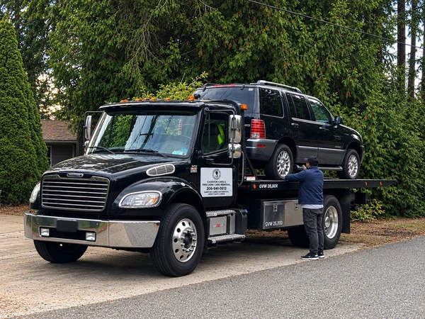 Black flatbed tow truck loading a dark SUV in a driveway