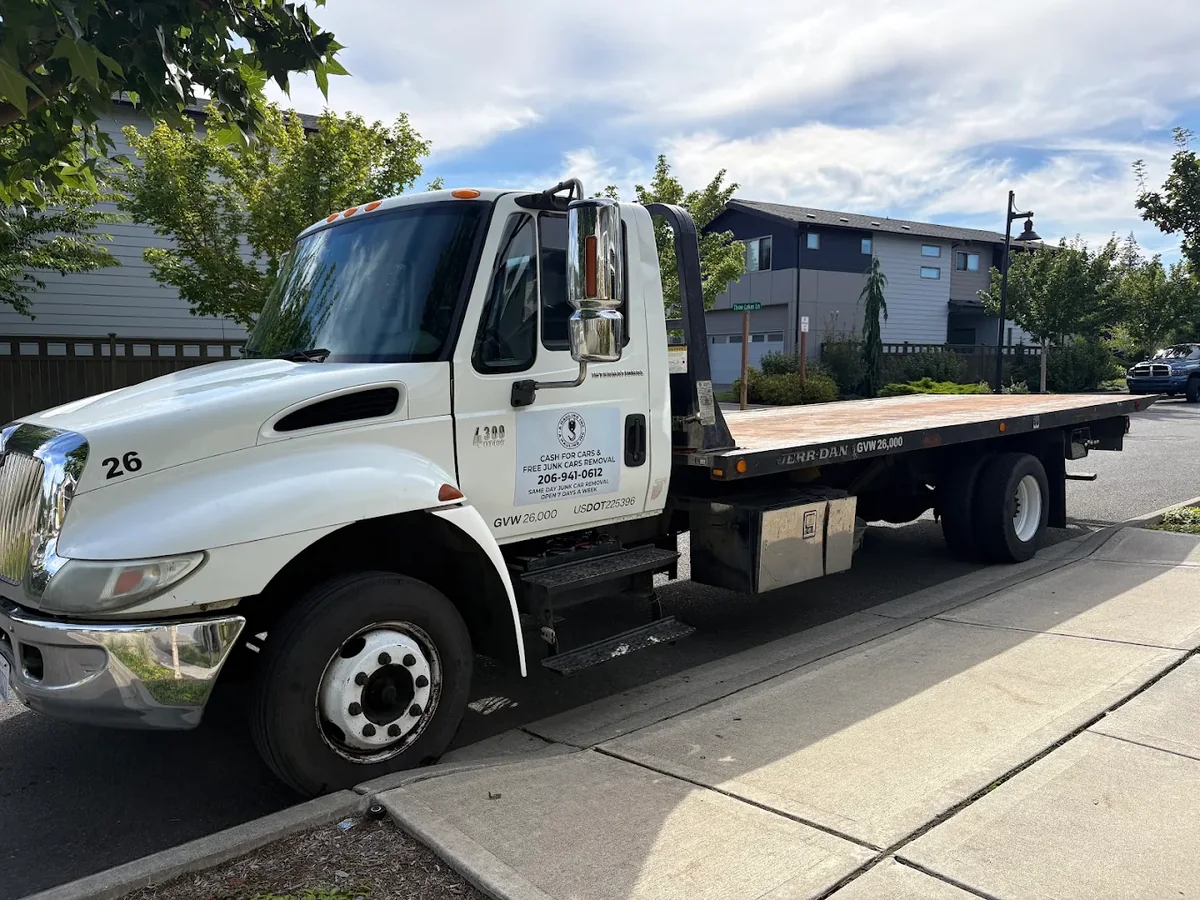 White Free Junk Car Hauling flatbed tow truck parked at the curb